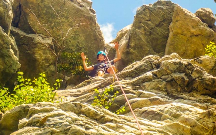 a student waves from above while rock climbing near DC